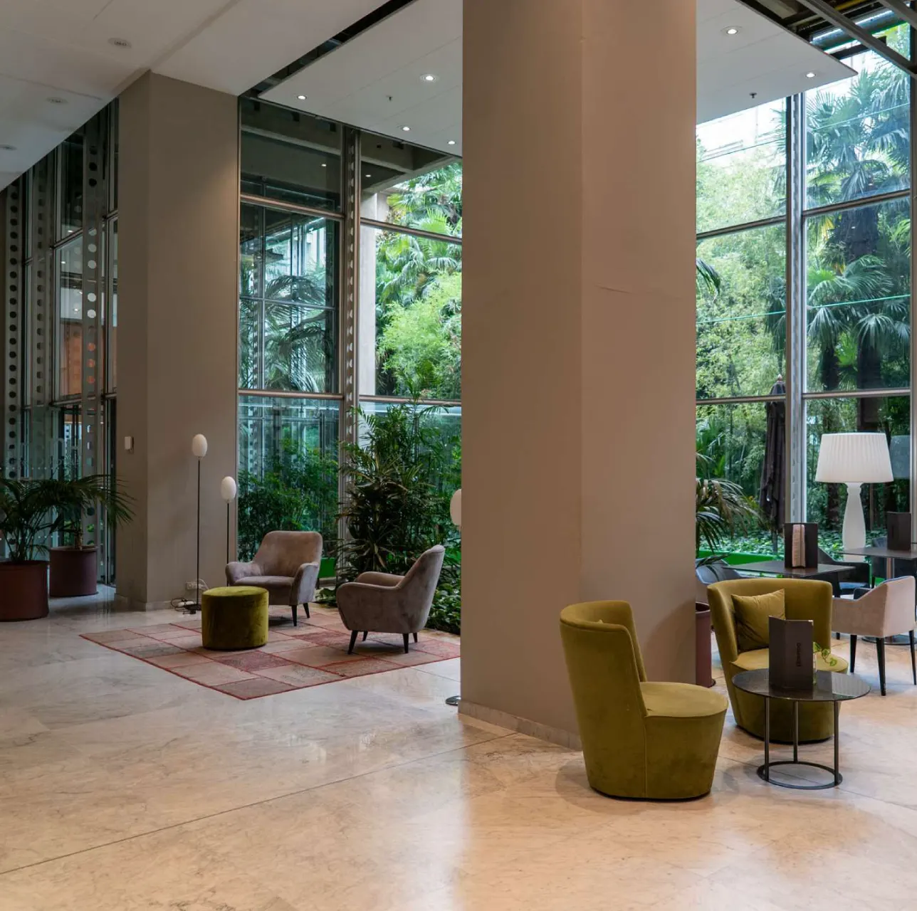 Lobby moderna di hotel o lounge Lingotto Torino con poltrone colorate, pareti vetrate e vista sul giardino interno.