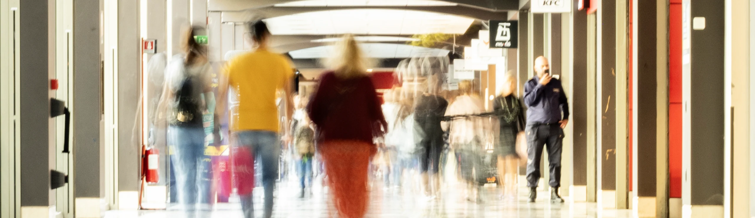Persone che camminano nel corridoio di centro commerciale, atmosfera urbana, movimento sfocato.