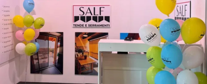 Stand espositivo SALF tende e serramenti con immagini di porte, finestre e palloncini colorati per la nuova apertura.